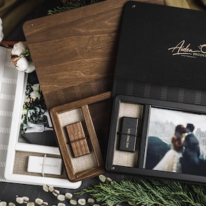 May include: A collection of wooden and black presentation boxes, some open to reveal photographs and USB drives. The boxes are branded with the text "Aiden Brooks Photography" in gold script. The image includes a wedding photo.