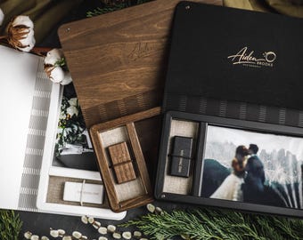 May include: A collection of wooden and black presentation boxes, some open to reveal photographs and USB drives. The boxes are branded with the text "Aiden Brooks Photography" in gold script. The image includes a wedding photo.