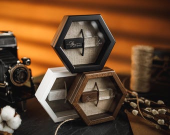 Puede incluir: Tres cajas de exhibición hexagonales en negro, blanco y marrón, apiladas una encima de la otra. Cada caja contiene un objeto pequeño y rectangular con texto escrito. Una cámara vintage y una flor de algodón están en primer plano.