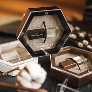 Puede incluir: Cajas hexagonales para unidades USB en negro, blanco y marrón. Cada caja contiene una unidad USB con la palabra "love" y la fecha de la boda 19/09/26. Las cajas se exhiben sobre una superficie oscura con elementos decorativos.