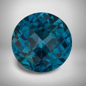 Puede incluir: Una gema redonda y facetada en tonos turquesa y turquesa. La gema tiene un corte brillante, con numerosas facetas pequeñas que crean un efecto brillante. La piedra se coloca sobre un fondo neutro, resaltando su color y claridad.
