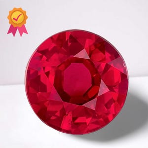 May include: A faceted, round-cut ruby gemstone. The gem is a deep, vibrant red colour, with multiple facets that reflect light. A gold seal with a checkmark and pink ribbons is in the upper left corner.
