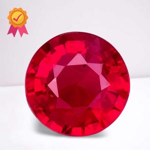 Könnte beinhalten: Ein facettierter, runder Rubin-Edelstein. Der Edelstein hat eine tiefe, satte rote Farbe mit mehreren Facetten, die das Licht reflektieren. Ein goldenes Siegel mit einem Häkchen und rosa Bändern befindet sich in der oberen linken Ecke.