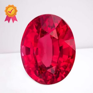 May include: A faceted, oval-shaped, deep red gemstone. The gem has a brilliant cut, reflecting light across its many facets. A gold seal with a checkmark and pink ribbons is in the upper left corner.
