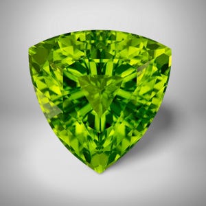 May include: A faceted, triangular-shaped gemstone with a vibrant, lime green color. The gem's intricate cuts create a dazzling display of light and shadow, showcasing its clarity and brilliance. The gemstone is set against a soft, neutral background.