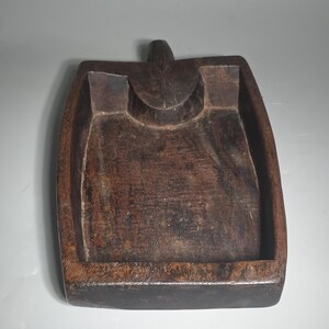 Könnte beinhalten: Ein rechteckiges, dunkelbraunes Holztablett mit Griff und geschwungener Vertiefung. Das Tablett hat einen erhöhten Rand und ein geschnitztes Design. Die Holzmaserung ist sichtbar und verleiht ihm ein rustikales Aussehen. Das Tablett ist wahrscheinlich handgefertigt.