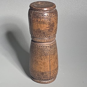 Puede incluir: Un recipiente de madera vintage con tapa. El recipiente cilíndrico presenta bandas decorativas talladas en la parte superior e inferior. La madera tiene un tono marrón cálido, con vetas visibles y signos de edad.