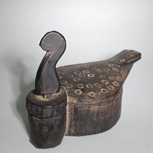 May include: A dark brown, handcrafted wooden box shaped like a bird, with a matching lid and a separate, cylindrical piece. The bird-shaped box has a textured surface with circular indentations. The cylindrical piece has a curved handle.