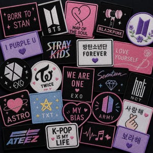 Puede incluir: Una colección de parches de tela bordados con varios logotipos, símbolos y frases de grupos de K-pop en rosa, morado, negro y blanco. Los diseños incluyen iconos como corazones, estrellas y notas musicales, con textos como BORN TO STAN, BTS, BLACKPINK y LOVE YOURSELF.