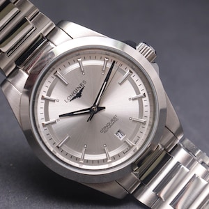 May include: A silver Longines Conquest automatic wristwatch with a stainless steel strap. The watch face is silver with black hands and hour markers. The date is displayed at the 3 o'clock position. A classic, elegant watch design.