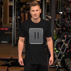 May include: Black t-shirt featuring a gray square with two vertical lines, resembling a pause symbol. The shirt is made of a soft material and is being worn in a gym setting.