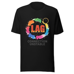 Op de afbeelding: Zwart t-shirt met een kleurrijk grafisch ontwerp. Het ontwerp bevat het woord "LAG" in oranje letters, omringd door gestileerde gamecontrollers in verschillende kleuren. De tekst "CONNECTION UNSTABLE" staat eronder.