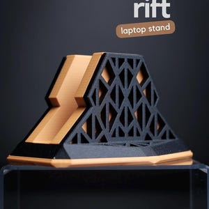 May include: A black and tan laptop stand with a geometric lattice design on the sides. The text "rift" appears in white above the words "laptop stand" in a brown rounded rectangle. The stand features a central slot for holding a device.