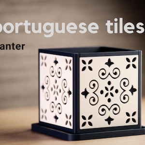 May include: A square black planter featuring white panels with intricate laser-cut scrollwork and floral patterns. The text "portuguese tiles" and "planter" appears in the upper left corner. The planter sits on a matching black square base.