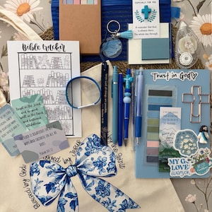 May include: A collection of religious stationery and accessories including a blue tote bag with a floral bow print, a Bible tracker sheet, a blue notebook with stickers, pens, a cross-shaped paperclip, sticky notes, and inspirational cards.