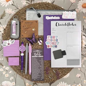 May include: A collection of stationery and accessories, including pens, stickers, and a notepad, arranged on a woven mat. The items are primarily purple and white, with the text "Church Notes" and "Trust in the Lord" visible. A lip balm is also included.