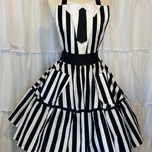 May include: A black and white striped apron with a white collar and black tie. The apron has a ruffled skirt and two pockets.