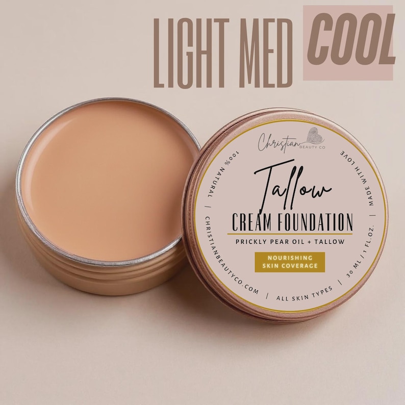 May include: Open, round, light-colored cream foundation in a metal tin. The label reads "Tallow Cream Foundation" with "Prickly Pear Oil + Tallow" and "Nourishing Skin Coverage." The text "Light Med Cool" is at the top.