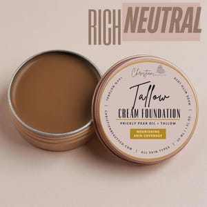 May include: Open tin of Rich Neutral Tallow Cream Foundation by Christian Beauty Co. The foundation is a light brown color. The tin is open, revealing the product. The label reads "Tallow Cream Foundation" and "Nourishing Skin Coverage."