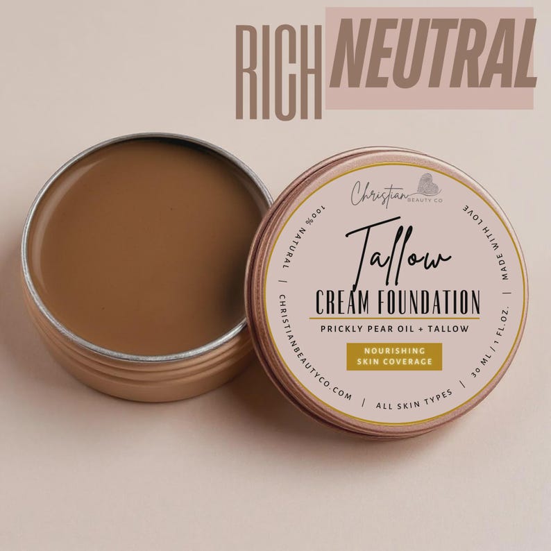 May include: Open tin of Rich Neutral Tallow Cream Foundation by Christian Beauty Co. The foundation is a light brown color. The tin is open, revealing the product. The label reads "Tallow Cream Foundation" and "Nourishing Skin Coverage."