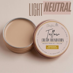May include: A light neutral cream foundation in a round, open tin. The tin is tan with a gold rim and has the text "Tallow Cream Foundation" and "Nourishing Skin Coverage". The text "Light Neutral" is at the top.