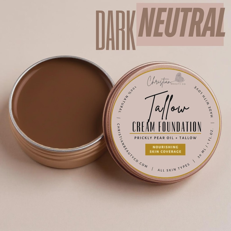 May include: An open, round, metal tin of dark neutral-toned cream foundation. The label reads "Tallow Cream Foundation" with "Prickly Pear Oil + Tallow" and "Nourishing Skin Coverage". The text "Dark Neutral" is at the top.