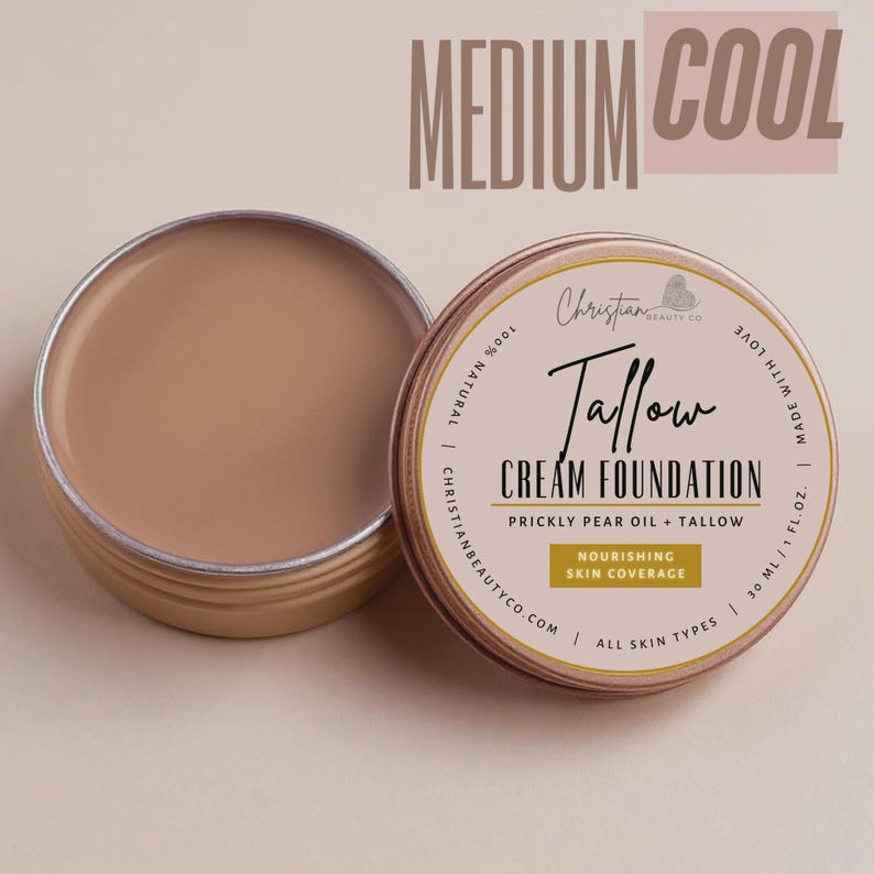May include: An open, round, metal container of medium cool-toned cream foundation next to a closed container. The closed container has text that reads "Tallow Cream Foundation" and "Nourishing Skin Coverage".
