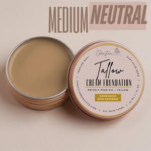 May include: Open tin of medium neutral Tallow Cream Foundation with a matching closed tin. The product is made by Christian Beauty Co. and contains prickly pear oil and tallow. The text on the tin reads "Nourishing Skin Coverage" and "All Skin Types".