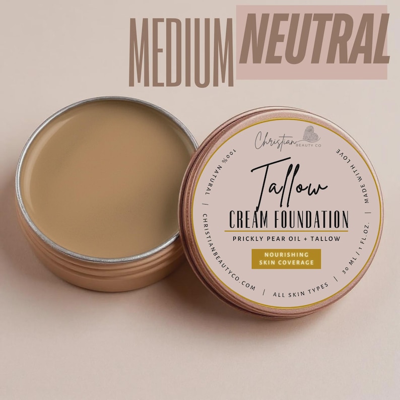 May include: Open tin of medium neutral Tallow Cream Foundation with a matching closed tin. The product is made by Christian Beauty Co. and contains prickly pear oil and tallow. The text on the tin reads "Nourishing Skin Coverage" and "All Skin Types".