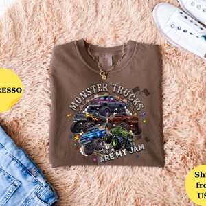 Peut inclure: T-shirt couleur expresso avec un motif de plusieurs monster trucks. Le texte "Monster Trucks Are My Jam" est affich&eacute; dans un design circulaire. Le t-shirt est associ&eacute; &agrave; un jean bleu et des baskets blanches.