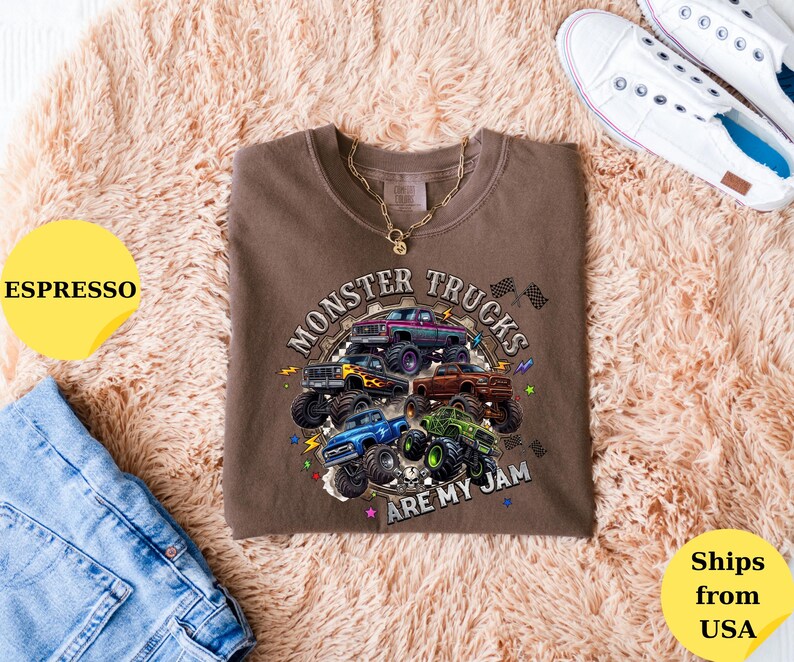 Peut inclure: T-shirt couleur expresso avec un motif de plusieurs monster trucks. Le texte "Monster Trucks Are My Jam" est affich&eacute; dans un design circulaire. Le t-shirt est associ&eacute; &agrave; un jean bleu et des baskets blanches.