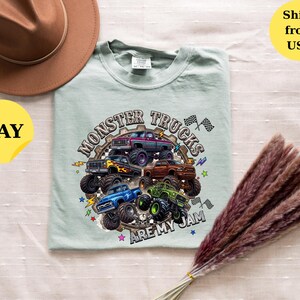 Peut inclure: T-shirt vert clair avec un motif de plusieurs monster trucks color&eacute;s et le texte "MONSTER TRUCKS ARE MY JAM". Un chapeau marron est dans le coin sup&eacute;rieur gauche.