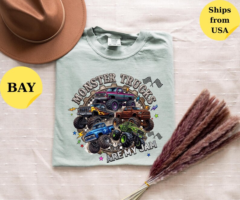 Peut inclure: T-shirt vert clair avec un motif de plusieurs monster trucks color&eacute;s et le texte "MONSTER TRUCKS ARE MY JAM". Un chapeau marron est dans le coin sup&eacute;rieur gauche.