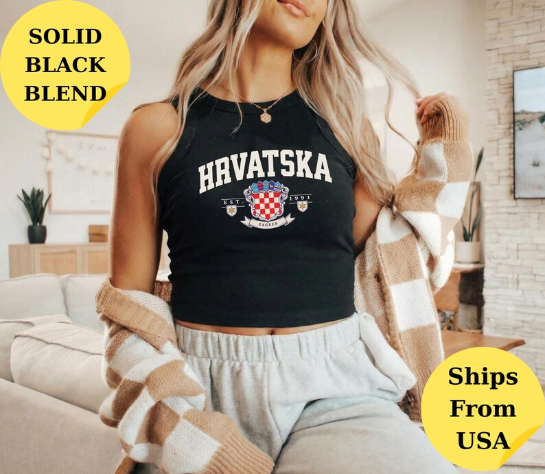 May include: A black sleeveless tank top featuring the white text HRVATSKA in an arched font above a graphic of the Croatian coat of arms with the text EST. 1991. The garment is worn with a beige and white checkered cardigan and light gray sweatpants.