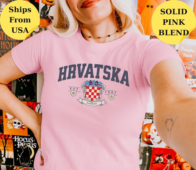 May include: A light pink short-sleeve t-shirt featuring the dark blue text HRVATSKA arched above a colorful coat of arms emblem. The emblem includes a red and white checkered shield, the text EST. 1991, and a banner with the word ZAGREB.
