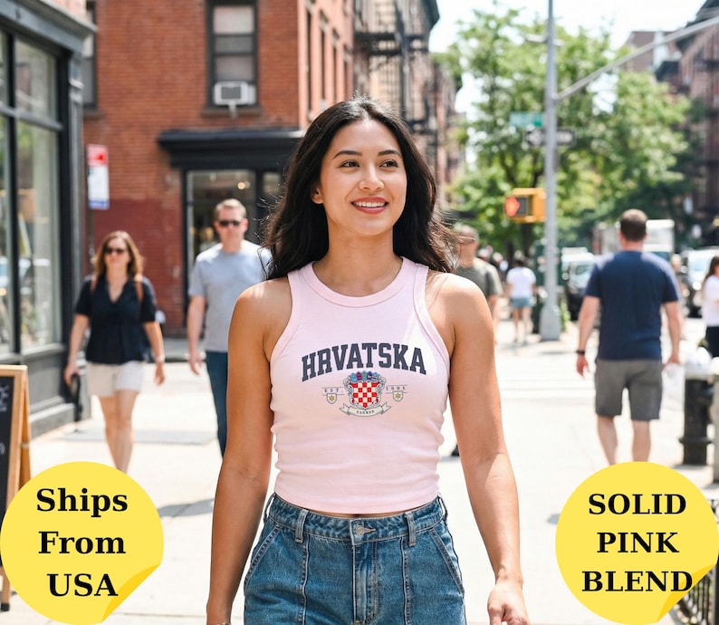 May include: A light pink sleeveless tank top featuring the text HRVATSKA in dark blue letters above a crest with a red and white checkered pattern. The garment has a ribbed texture and a high neckline, paired with blue denim jeans.