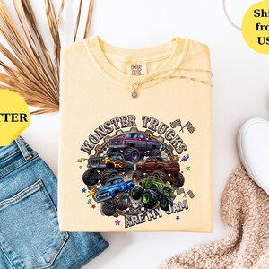 Peut inclure: T-shirt jaune beurre avec un motif de monster trucks multicolores et l'inscription "MONSTER TRUCKS ARE MY JAM". Le t-shirt est pr&eacute;sent&eacute; avec un jean bleu et des chaussures blanches.
