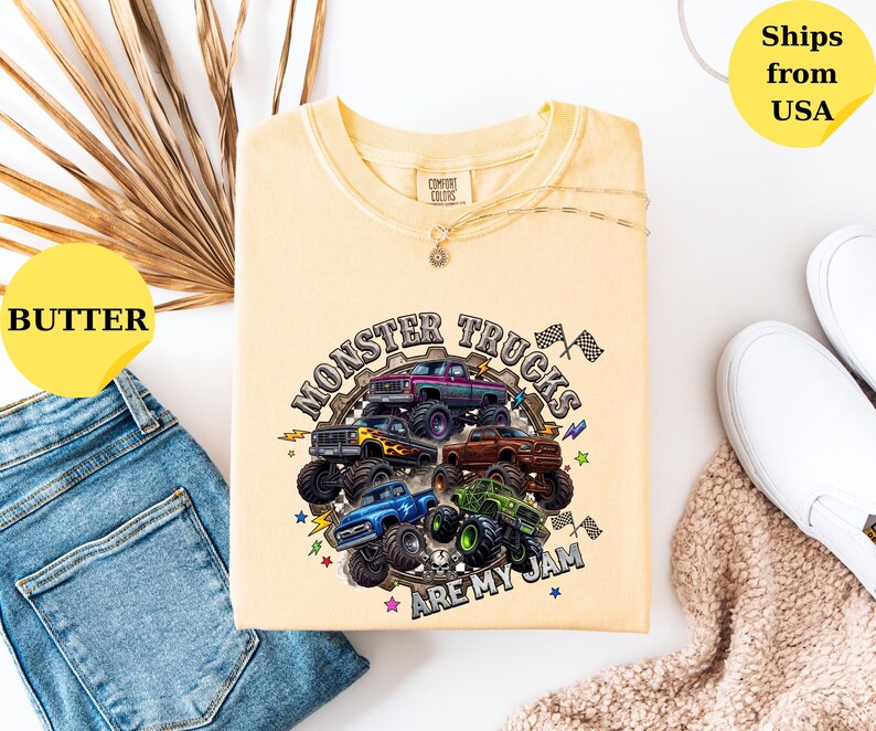 Peut inclure: T-shirt jaune beurre avec un motif de monster trucks multicolores et l'inscription "MONSTER TRUCKS ARE MY JAM". Le t-shirt est pr&eacute;sent&eacute; avec un jean bleu et des chaussures blanches.