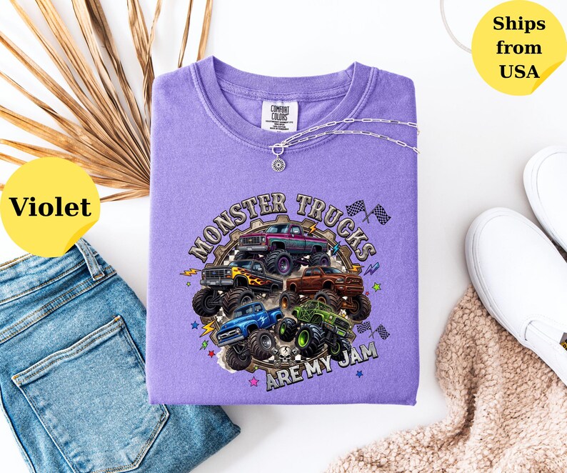 Peut inclure: Un t-shirt violet Comfort Colors avec un motif de monster trucks et le texte "MONSTER TRUCKS ARE MY JAM". Un collier argent&eacute; est drap&eacute; sur le t-shirt. Le t-shirt est pr&eacute;sent&eacute; avec un jean bleu et des chaussures blanches. Le t-shirt est d'une nuance de violet vif.