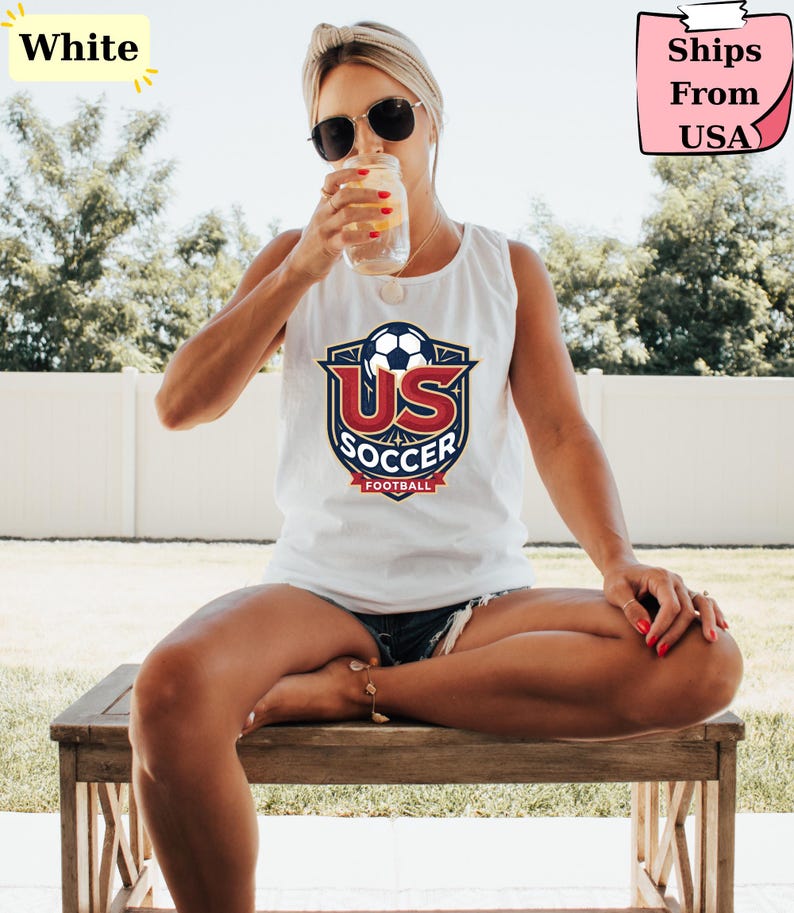 May include: A white sleeveless tank top featuring a graphic logo on the chest. The logo displays a soccer ball above the red text US and the blue text SOCCER, with the word FOOTBALL on a red banner at the bottom, all enclosed in a shield design.