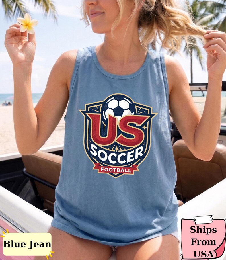 May include: A blue sleeveless tank top featuring a graphic emblem on the chest. The design includes a soccer ball above large red letters reading US, with the word SOCCER in white below, and a red banner at the bottom with the word FOOTBALL.
