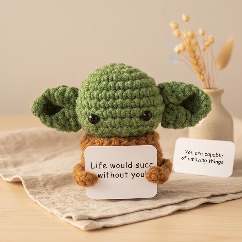 May include: A handmade crochet figure in the likeness of a popular character, with large ears and black eyes. The figure holds a card that reads "Life would succ without you!" and another card that reads "You are capable of amazing things."