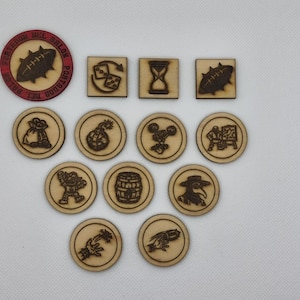 May include: A collection of wooden game tokens featuring laser-engraved icons. There are three square tiles and ten circular tokens, including one red-rimmed circular token with a football graphic and the text "PORTADORES DEL BALON".