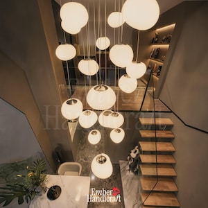 May include: A multi-pendant chandelier featuring numerous spherical white glass globes suspended at varying heights by thin cords. The fixture includes chrome hardware and illuminates the space with a soft glow, hanging above a marble table.