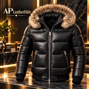 May include: A black puffer jacket with a shiny finish, featuring a hood trimmed with brown and tan faux fur. The jacket has a full-length silver front zipper, two zippered side pockets, and black ribbed cuffs. The text AP LeatherHide is visible.