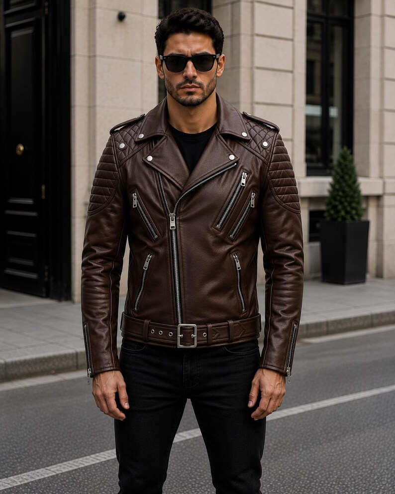 Man wearing chocolate brown leather biker jacket with quilted sleeves, asymmetrical front zipper and belted waist in an urban evening setting.