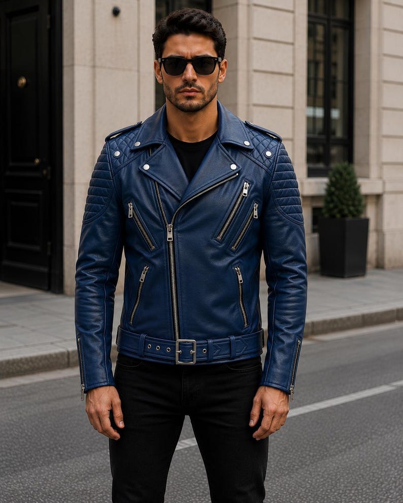 Man wearing blue leather biker jacket with quilted sleeves, asymmetrical front zipper and belted waist in an urban evening setting.