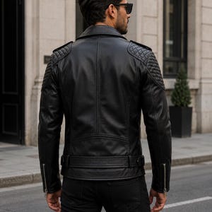 Man wearing black leather biker jacket with quilted sleeves, asymmetrical front zipper and belted waist in an urban evening setting.