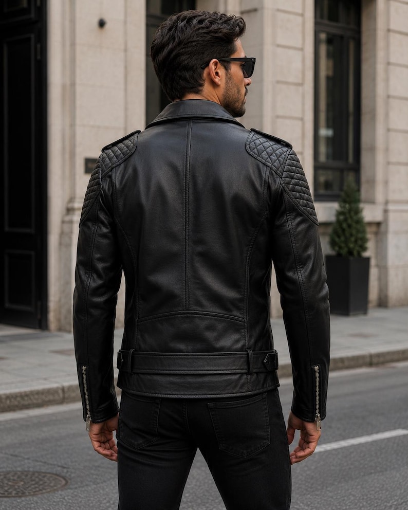 Man wearing black leather biker jacket with quilted sleeves, asymmetrical front zipper and belted waist in an urban evening setting.