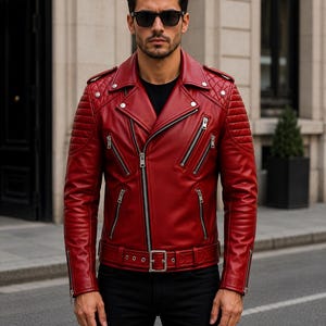 Man wearing red leather biker jacket with quilted sleeves, asymmetrical front zipper and belted waist in an urban evening setting.
